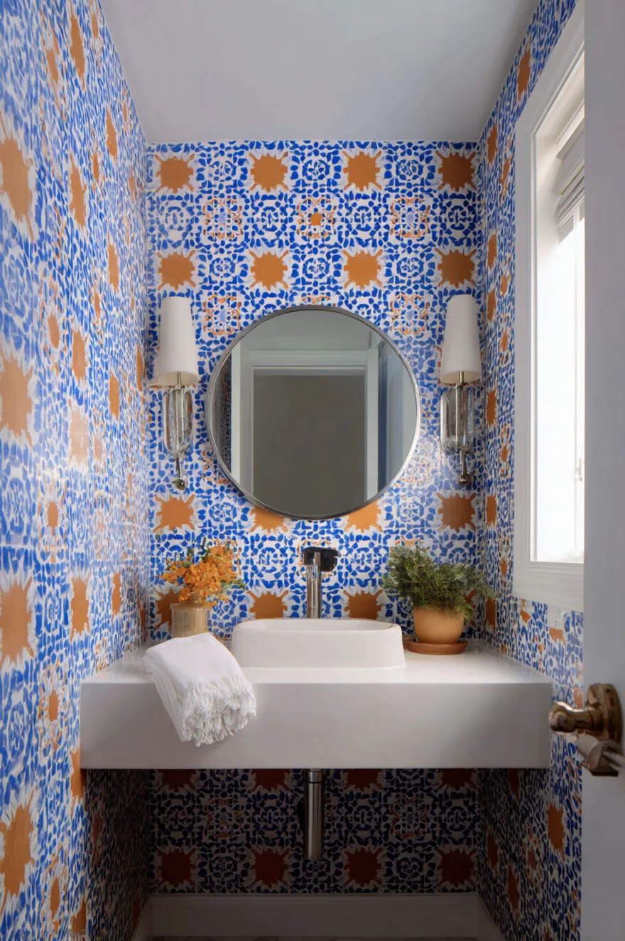 Powder room with terracotta and cobalt geometric encaustic tile covering walls and ceiling, white wall-hung sink, chrome faucet, and a round frameless mirror as visual anchor.